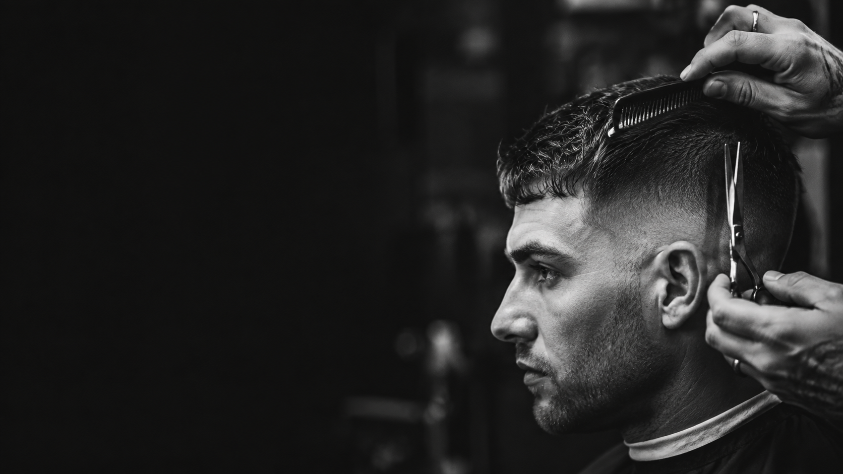 Black and white close-up of a barber cutting hair with scissors and a comb